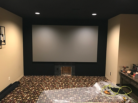 Home theater room with large screen, dark accents, and carpet under construction.