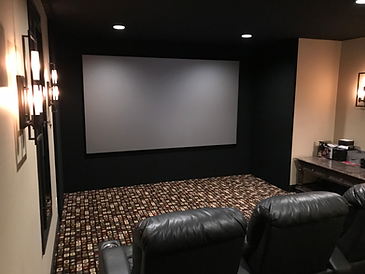 Home theater with black screen, leather recliners, and patterned carpet.