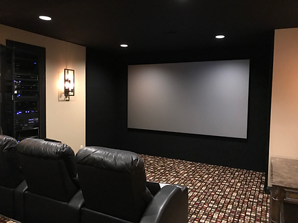 Home theater with a large screen, black walls, leather recliners, and patterned carpet.