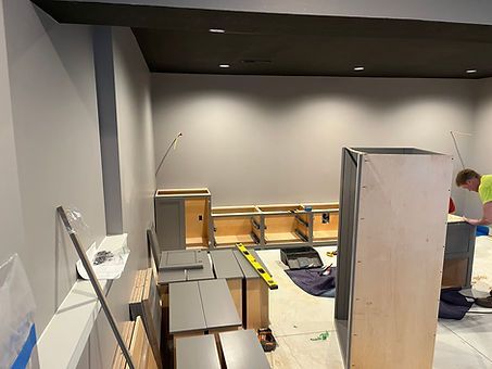 Cabinets being installed in a room with gray walls and black ceiling.