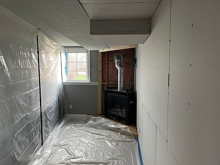 Basement room under construction: plastic sheeting on walls and floor, drywall partially installed, fireplace visible.