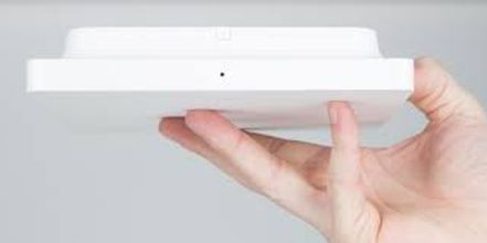 Hand holding a small white square electronic device against a gray background.