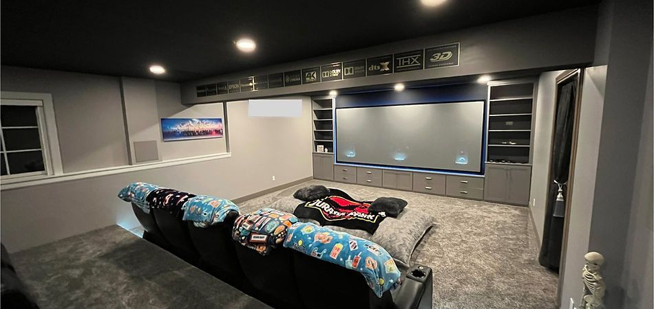 Home theater with gray walls, black ceiling, large screen, built-in cabinets, and a plush rug.