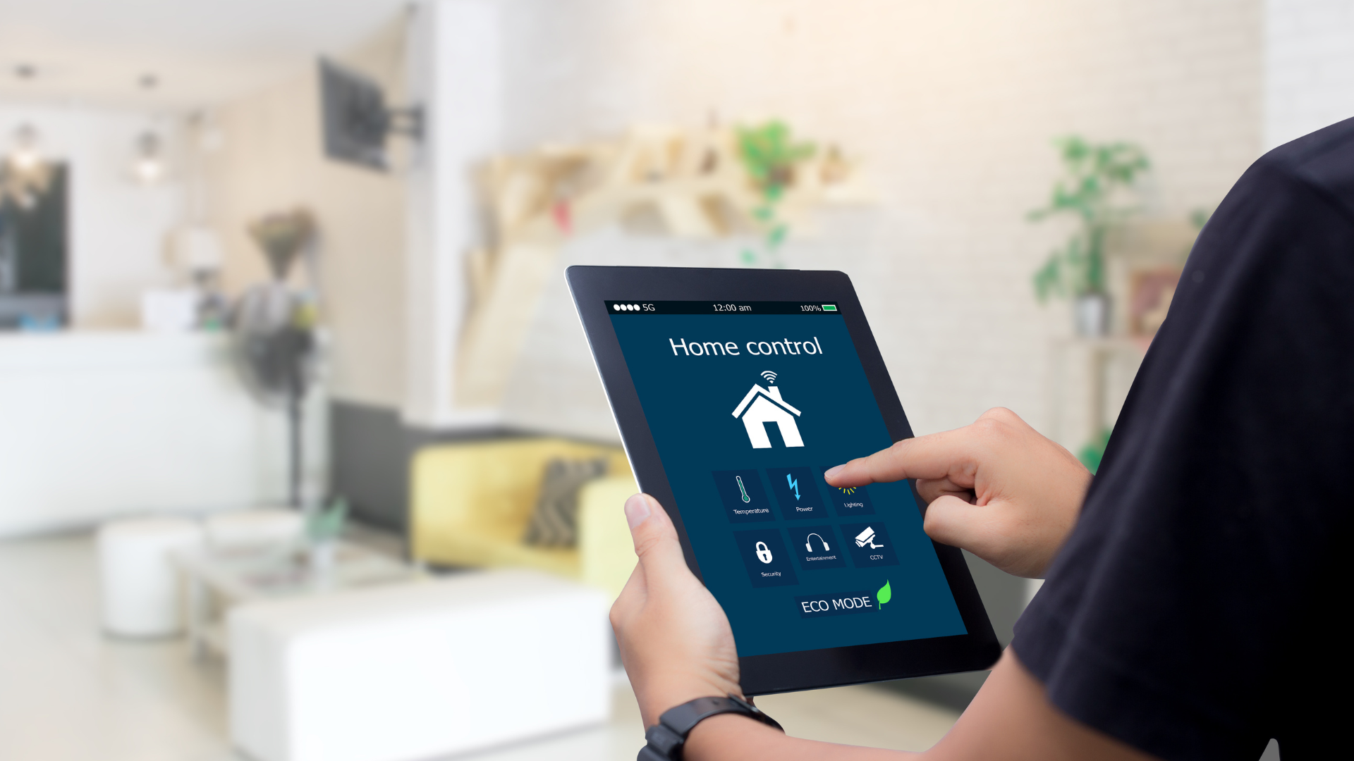 Person using a tablet to control a smart home system with a blurred living room background.