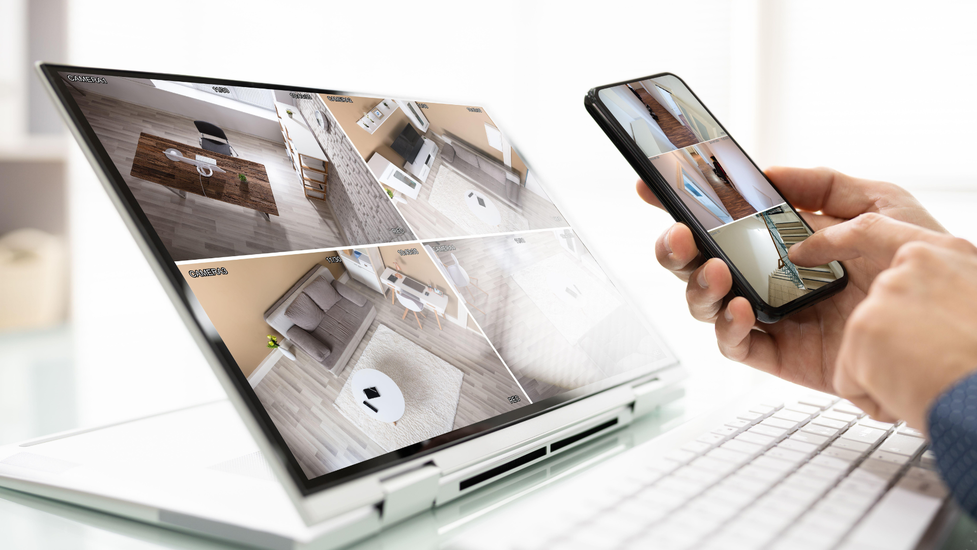 Person using laptop and smartphone to view security camera feeds.