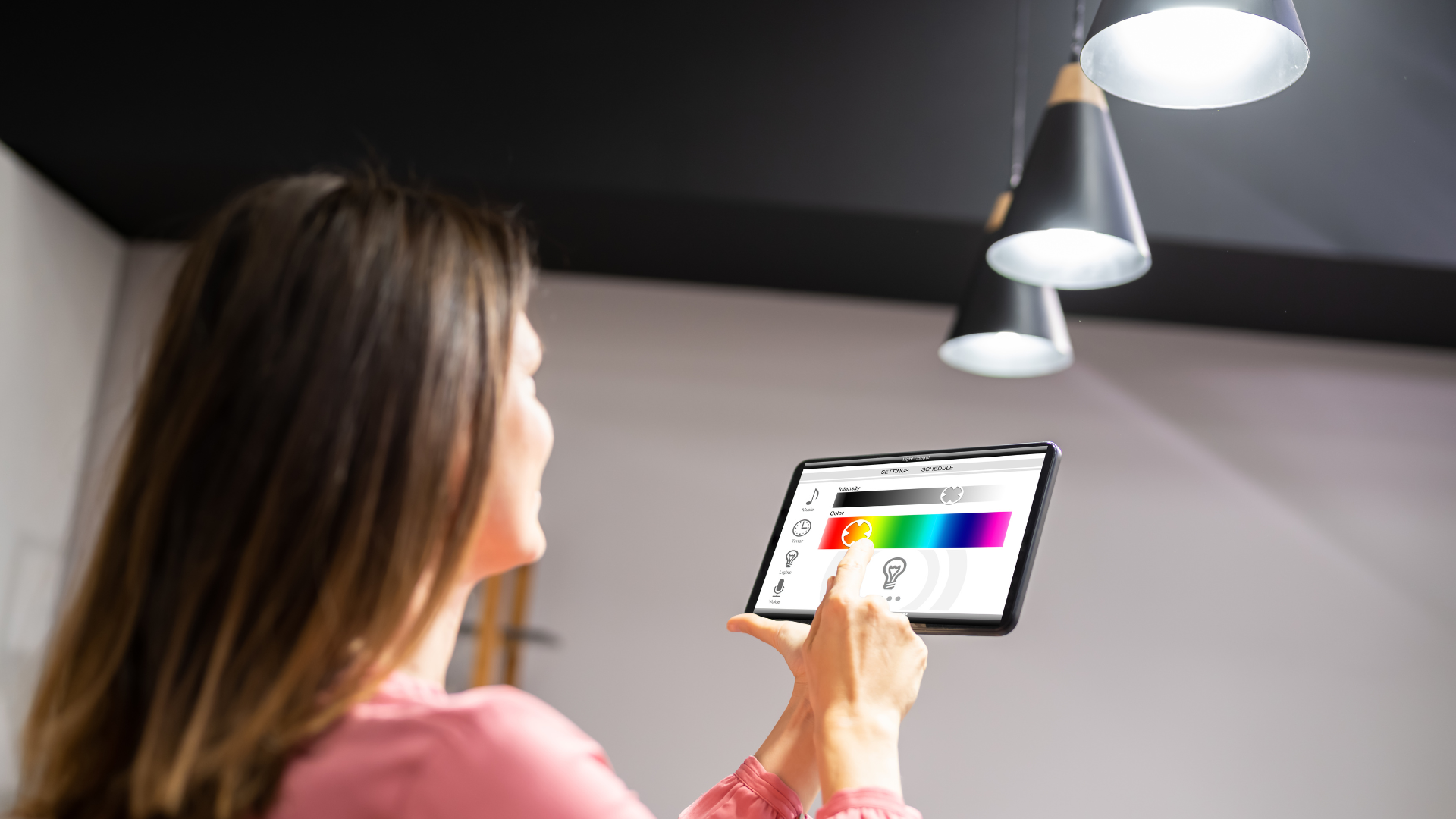 Woman adjusts smart lighting color on a tablet. Lights illuminate a dark ceiling, changing color.