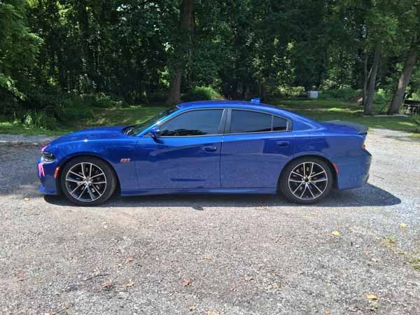 Blue Dodge Charger parked on gravel next to trees.
