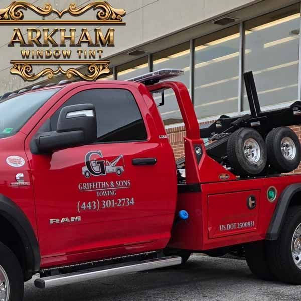 Red tow truck with tinted windows parked outside a building, logo reading 