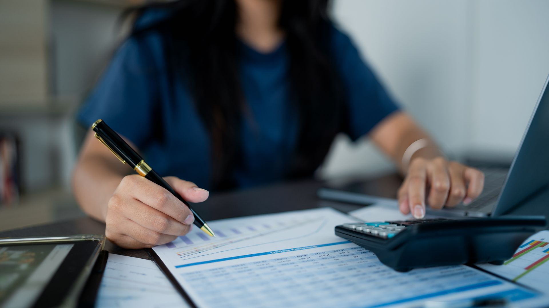 A woman is sitting at a desk with a pen and calculator.