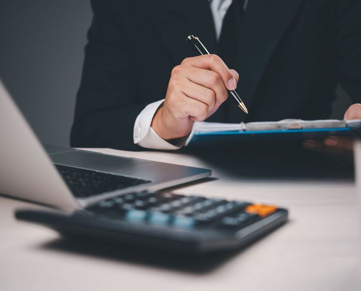 A man is sitting at a desk holding a pen and a clipboard.