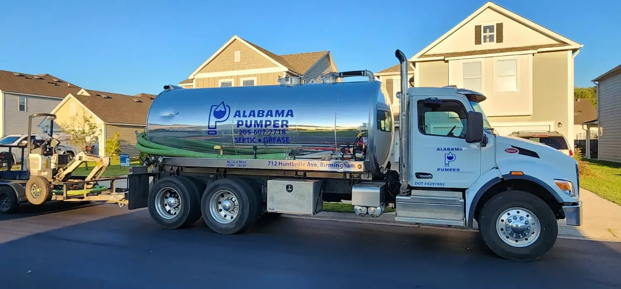 A septic tank truck is parked in front of a house with a green hose attached to it.