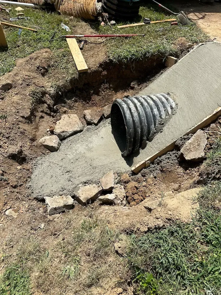 Concrete drainage project with pipe, framed by wood planks and rocks, in a grassy yard.