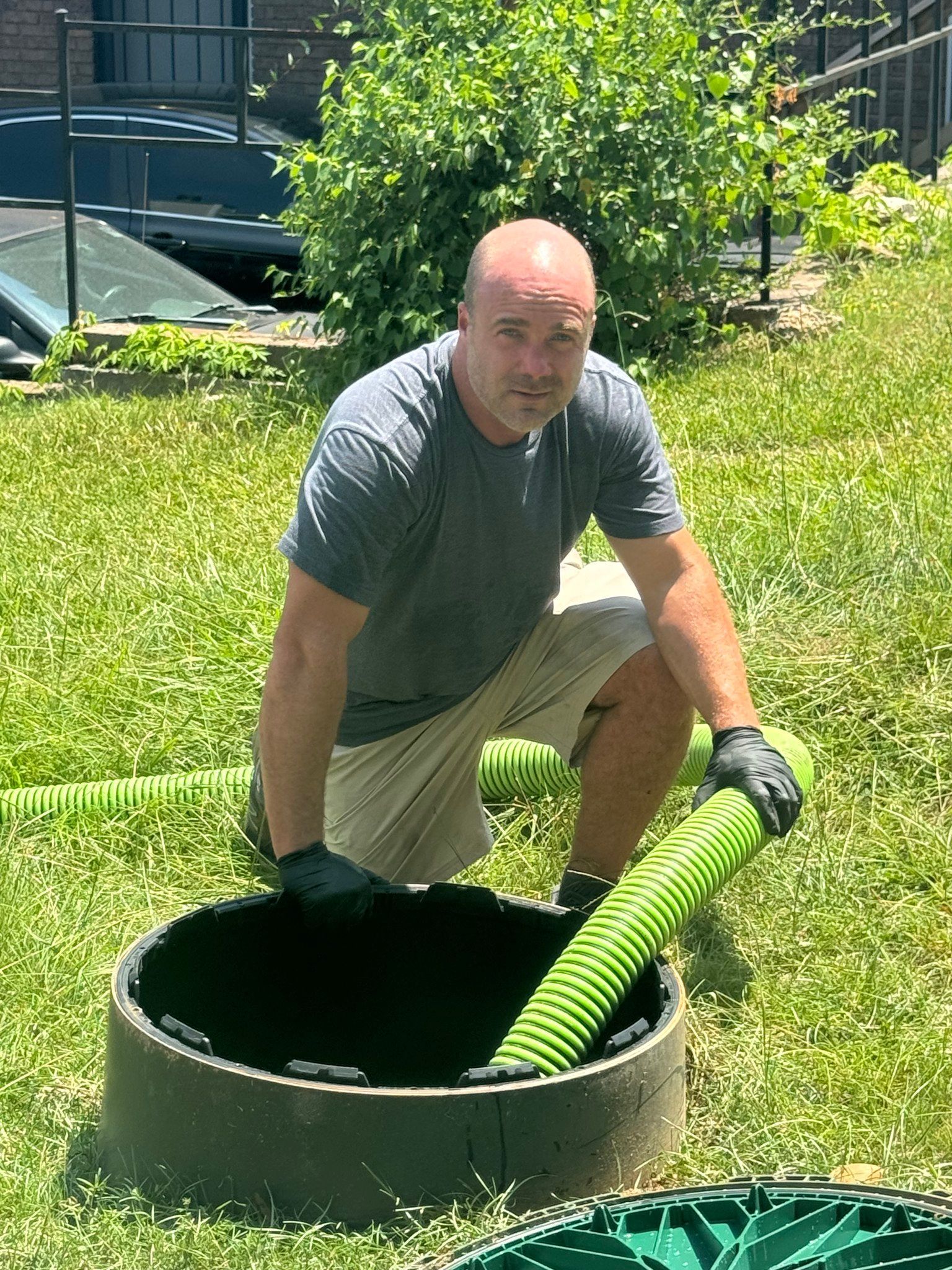 Alabama Pumper Owner Jay Hancock is kneeling down in the grass next to a septic tank.
