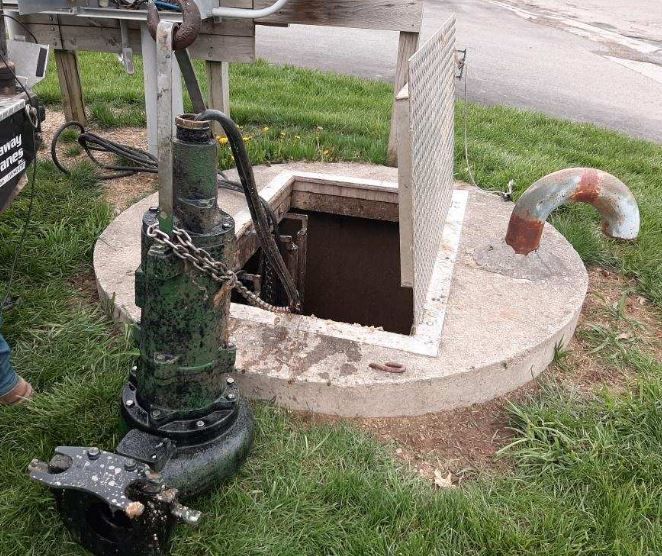Green septic pump positioned near a lift station manhole cover during routine maintenance in Odenville Alabama.