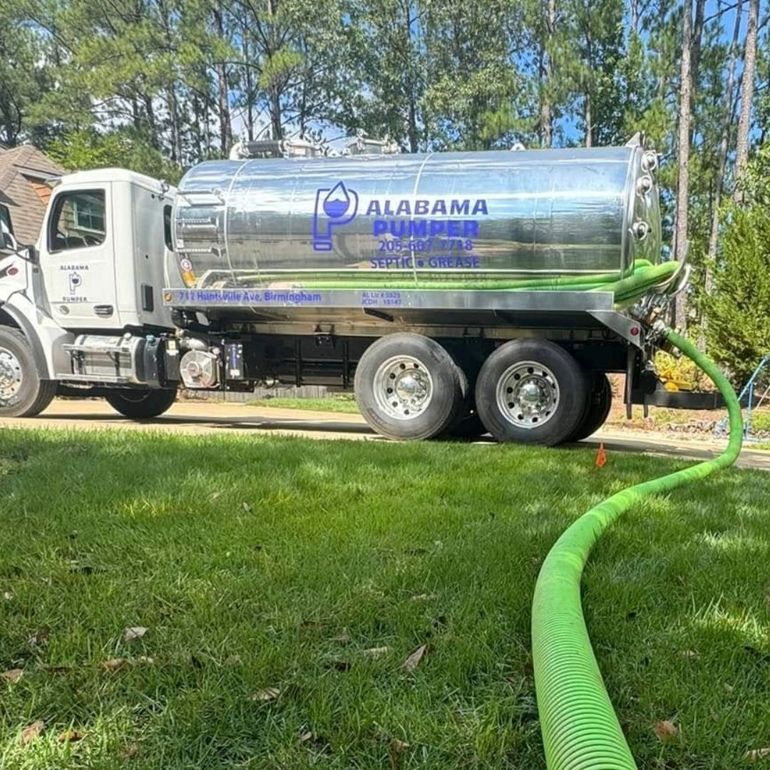 A septic tank truck is parked in front of a house with a green hose attached to it.