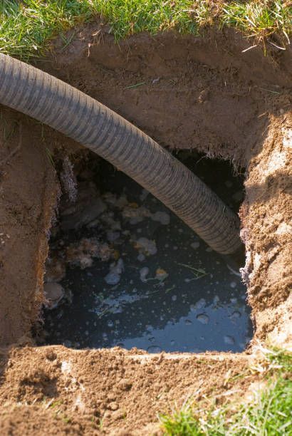 Excavated square hole with muddy water and a black corrugated hose leading into it.
