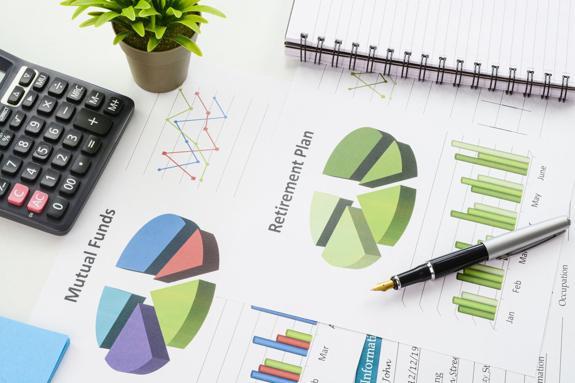 Calculator, financial charts, pen, and notepad on a white desk, suggesting finance or planning.