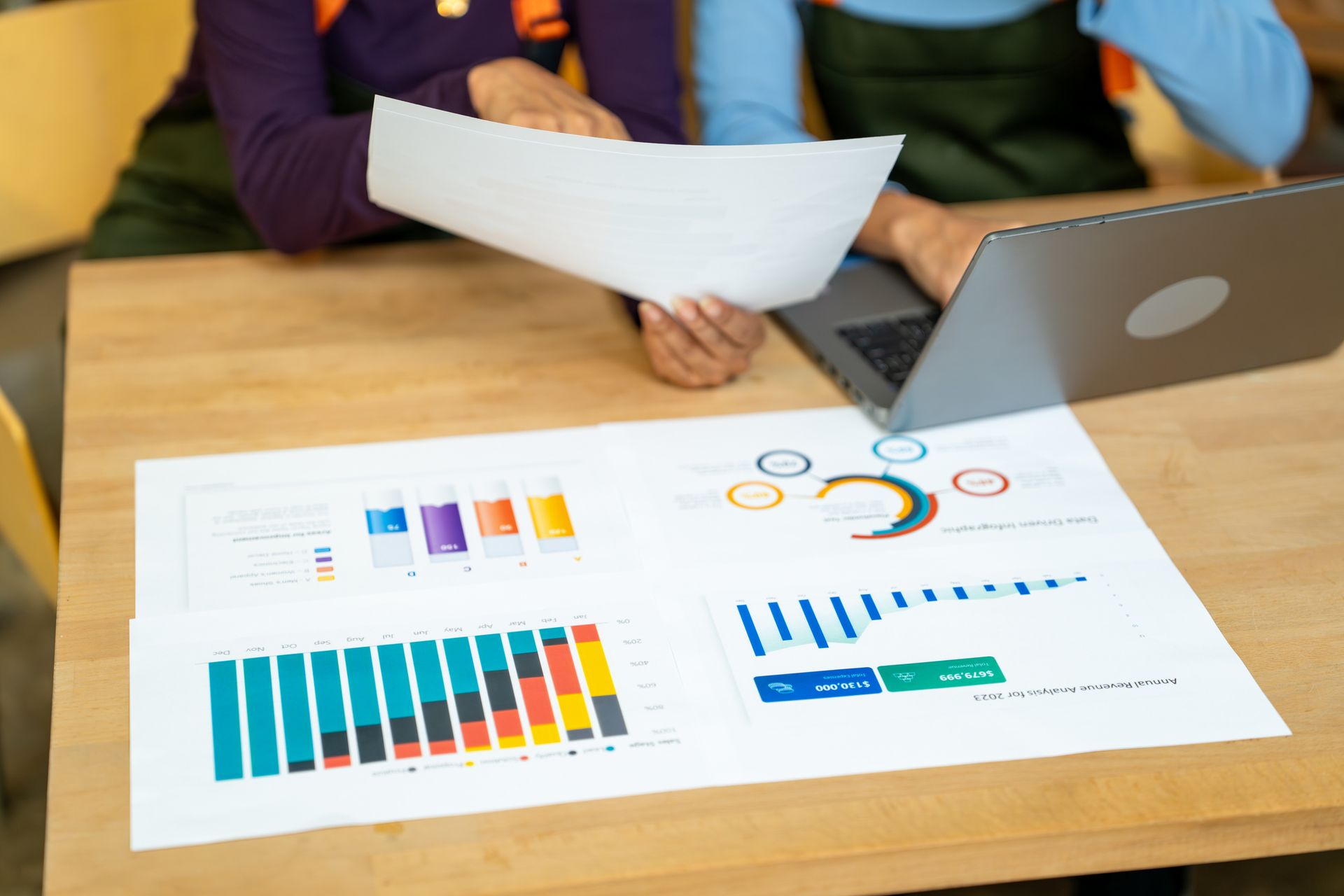 People reviewing charts and graphs on a table with a laptop.