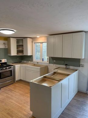 A kitchen under renovation with white cabinets, a central island, and a stainless steel stove on a hardwood floor.