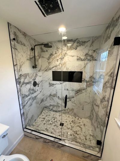 A walk-in shower with white and grey marble tile walls, a matte black shower head, and a glass door in a bathroom.