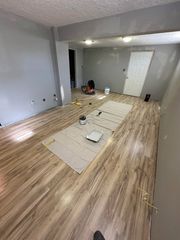 A room under renovation with new wood-look flooring, grey walls, and painting supplies placed on protective floor paper.