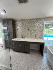 Modern bathroom with a dark wood vanity, white countertop, patterned tile backsplash, and a glass shower door.