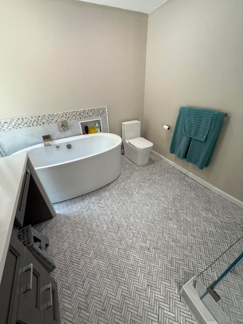 A modern bathroom with a freestanding white oval bathtub, a toilet, a glass-enclosed shower, and herringbone-patterned flooring.