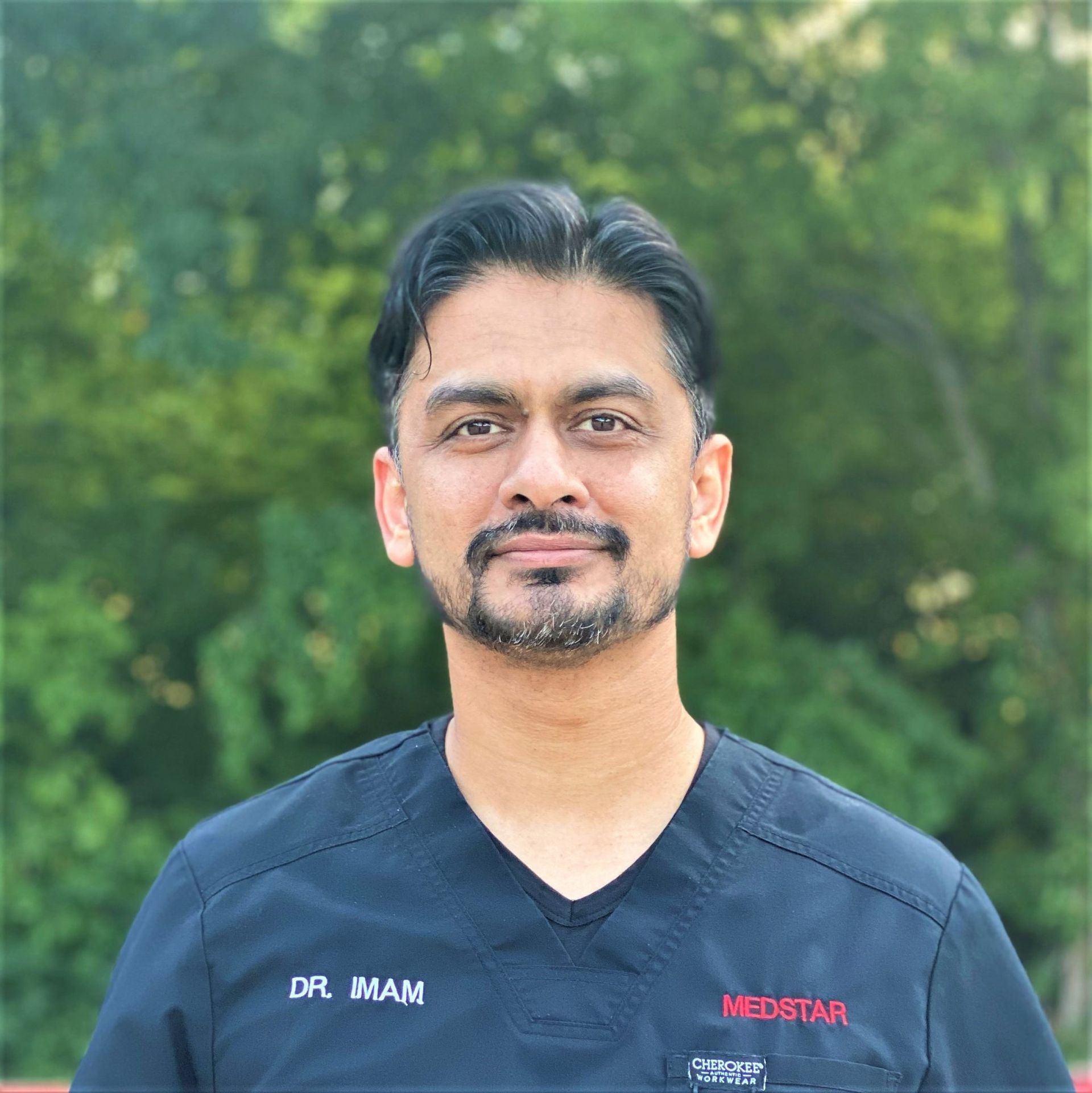 A man with a beard is wearing a black scrub top.
