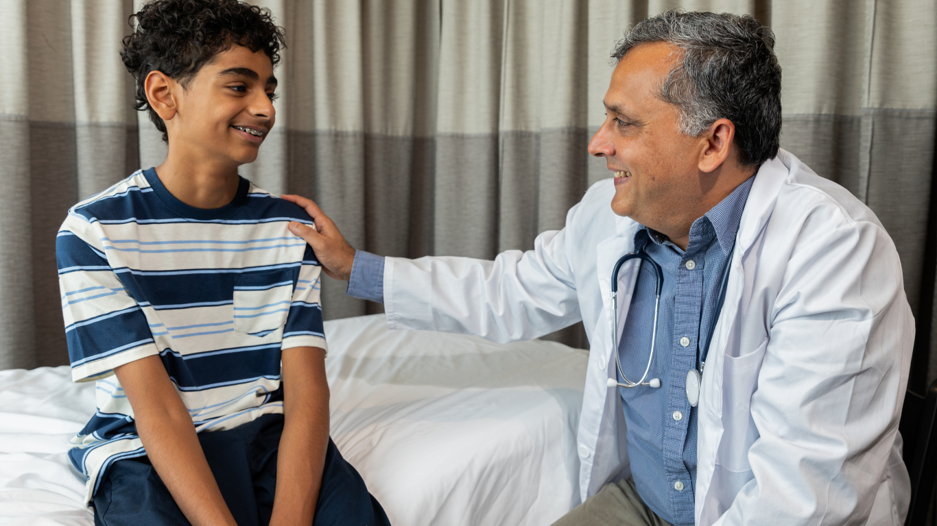 A doctor is talking to a young boy who is sitting on a bed.