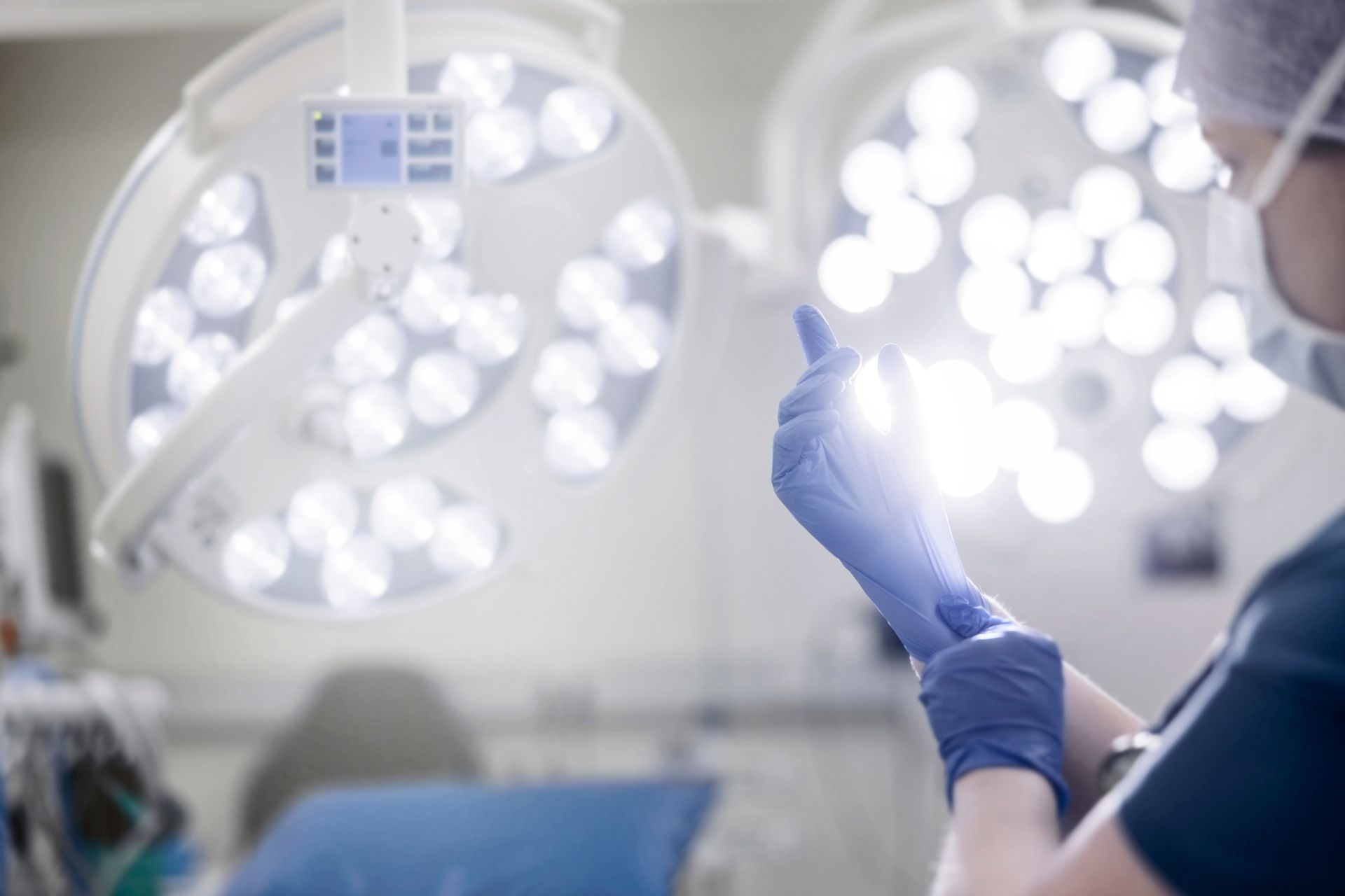 Surgeon putting on blue gloves in a brightly lit operating room.