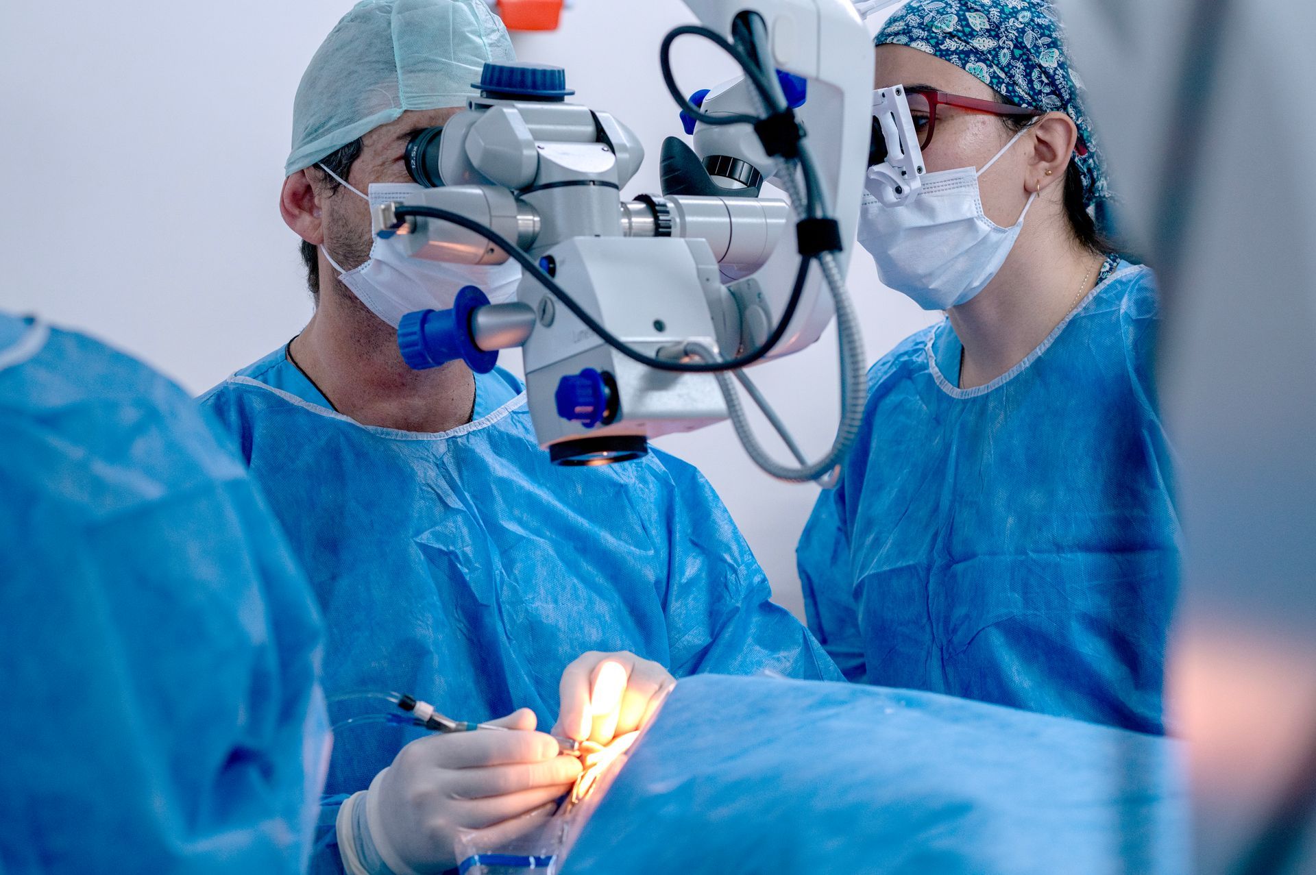 Surgeons performing eye surgery, one looking through microscope, assisted by another; operating room.