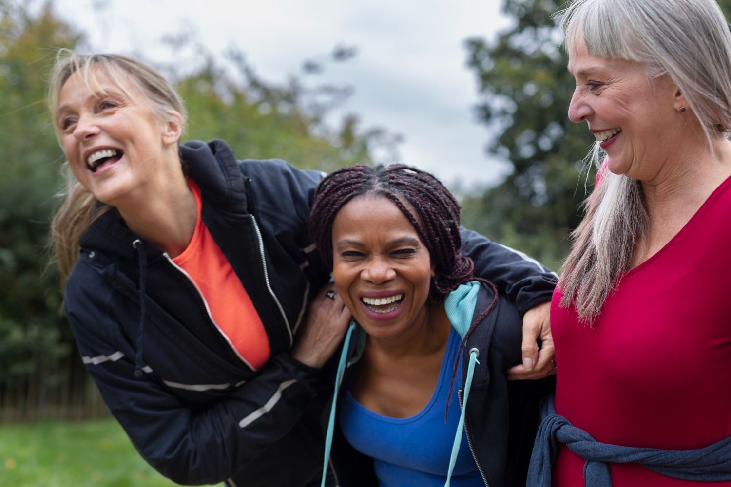 Three diverse women laughing outdoors, arm in arm.