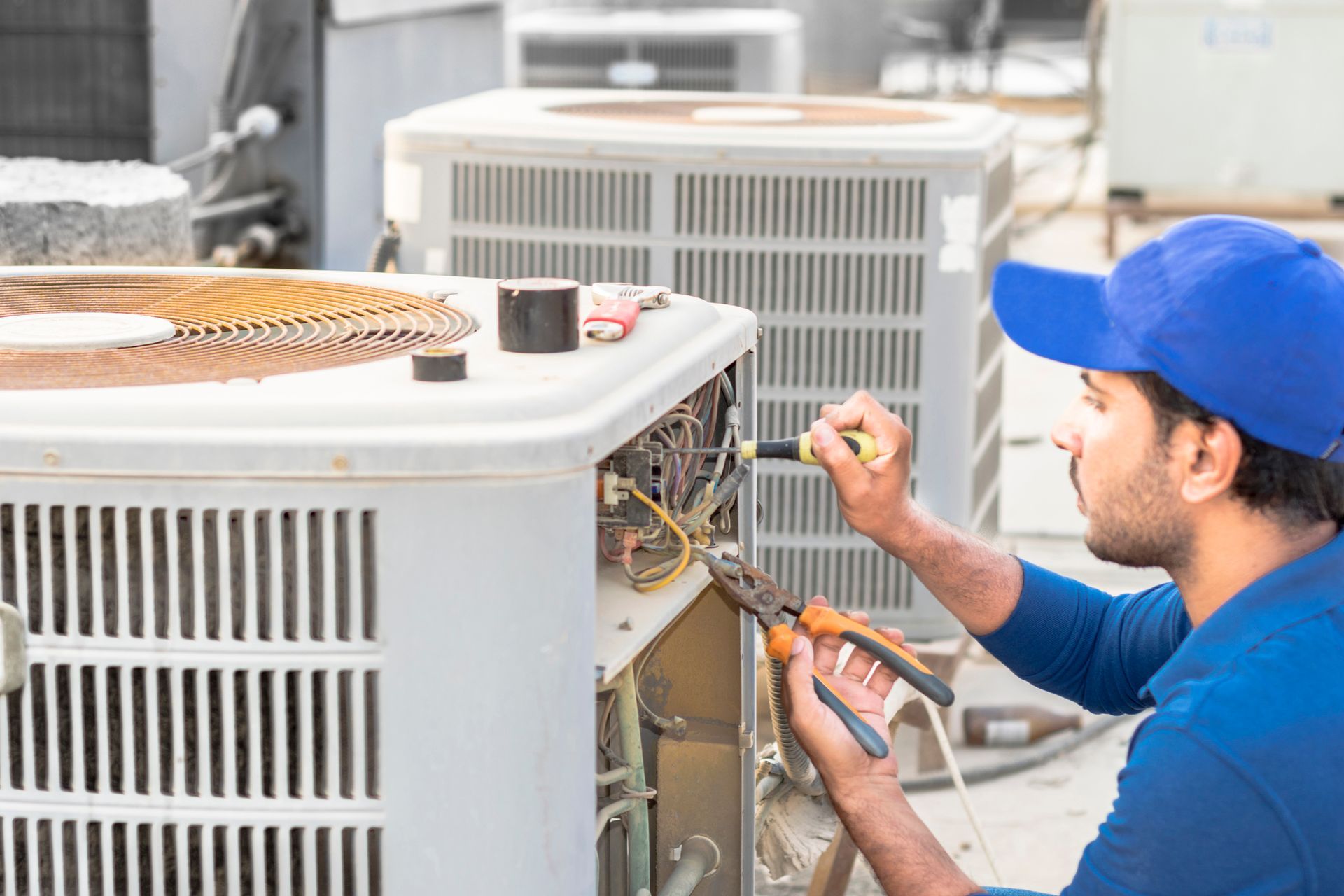A technician wearing blue uniform is performing commercial AC repair service on a building rooftop.