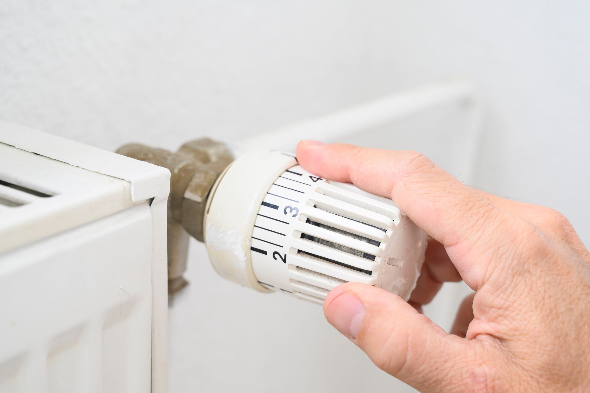 A man's hand adjusting the temperature of a radiator.