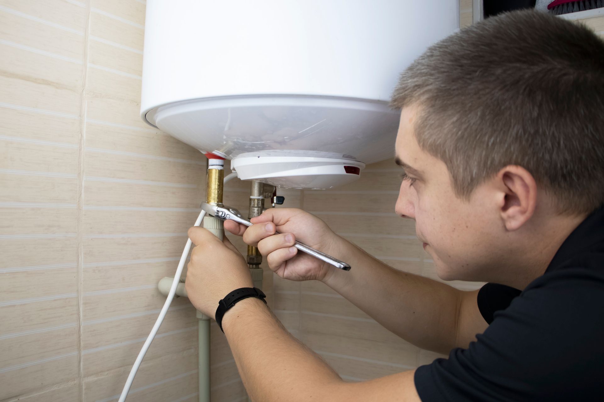 A male worker is repairing a water heater with a wrench. A male worker is repairing a water heater with a wrench.