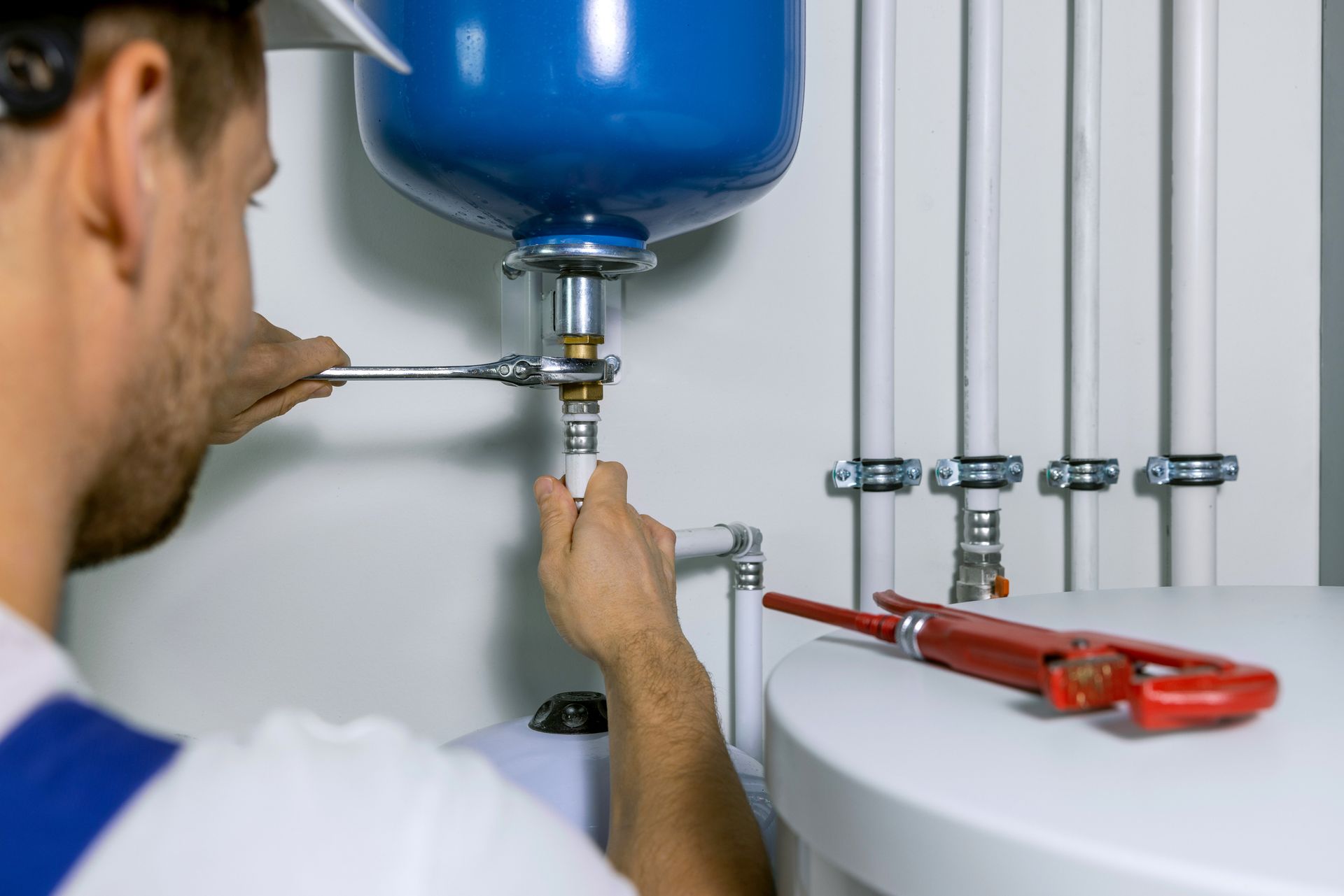 A male worker is tightening pipes under a blue water tank.