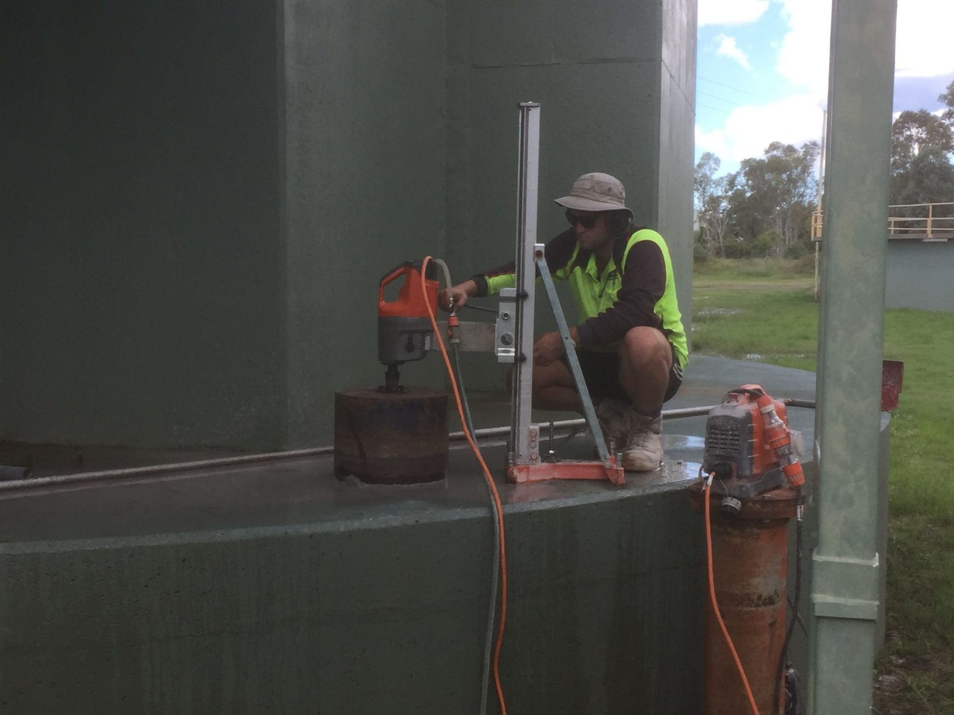 Worker Using a Core Drill on a Green Tank Outdoors — Dondarra Concrete Cutting & Drilling in Parkhurst, QLD