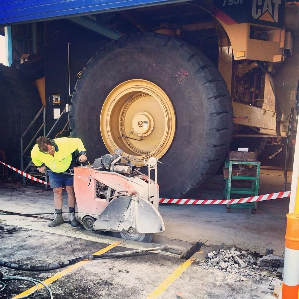 A Worker Cutting Concrete Near a Massive Yellow Tire — Dondarra Concrete Cutting & Drilling in Parkhurst, QLD