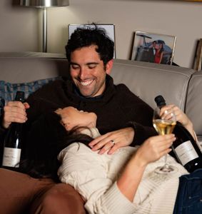 a couple enjoying their fizz champagne club bottles at home on the couch together.
