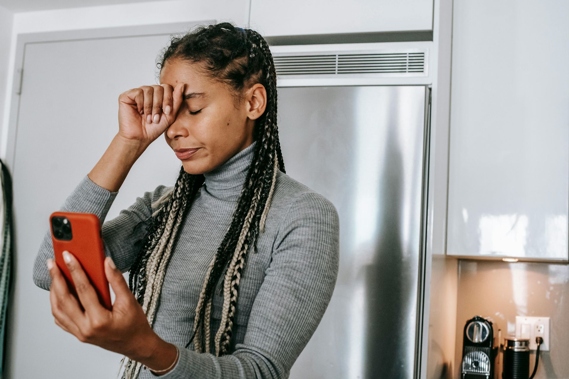 A woman is rubbing her eyes while looking at her cell phone.