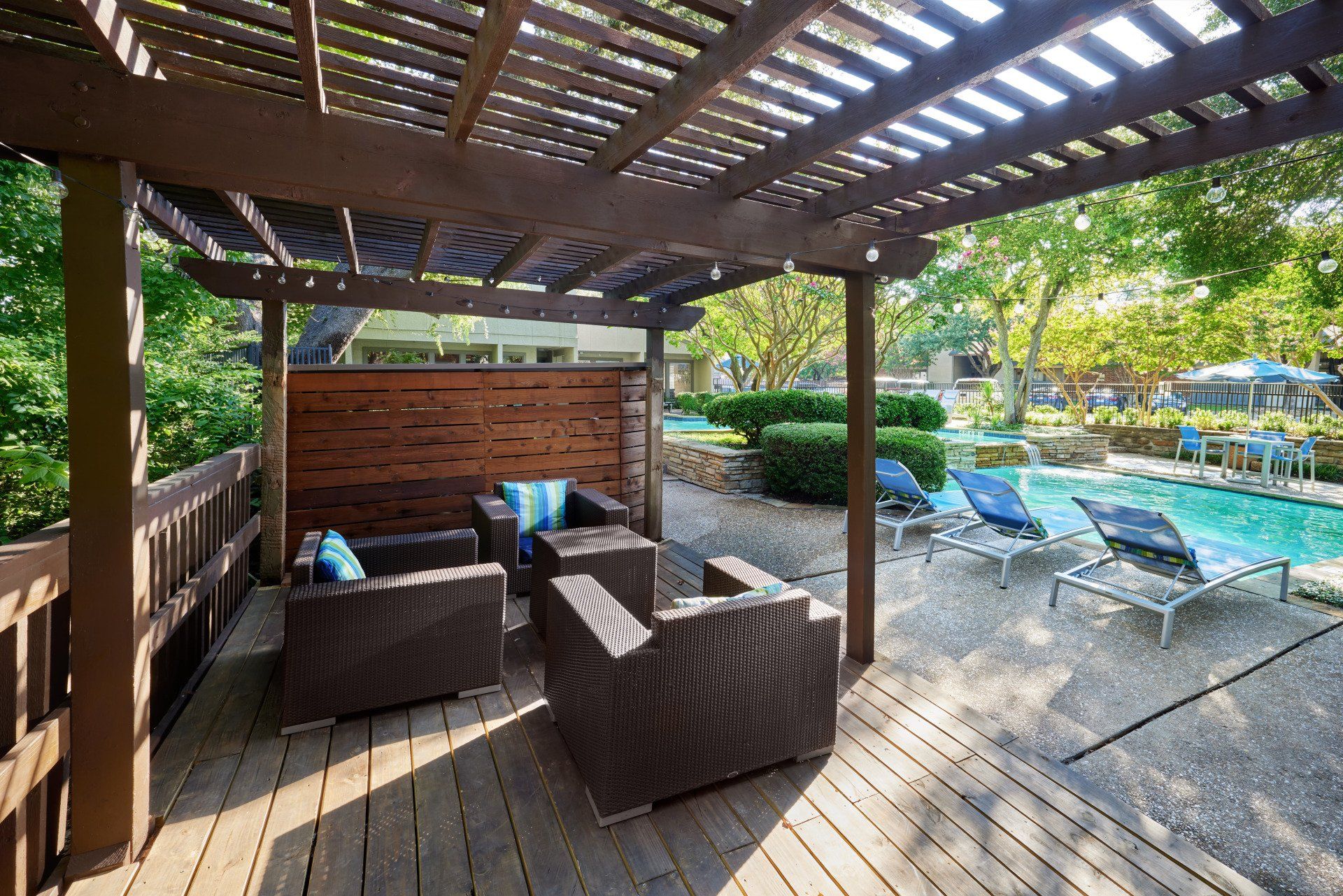 A wooden deck with chairs and a pergola overlooking a swimming pool at Summerwood Cove Apartments.