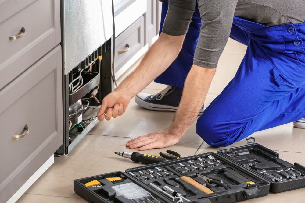 A Man Is Kneeling On The Floor Fixing A Refrigerator In A Kitchen — Climatech In Nambour, QLD