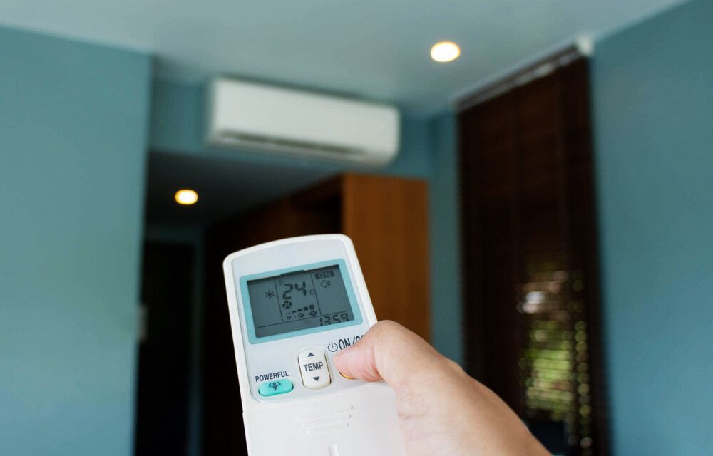 A Person Is Holding A Remote Control In Front Of An Air Conditioner — Climatech In Marcoola, QLD