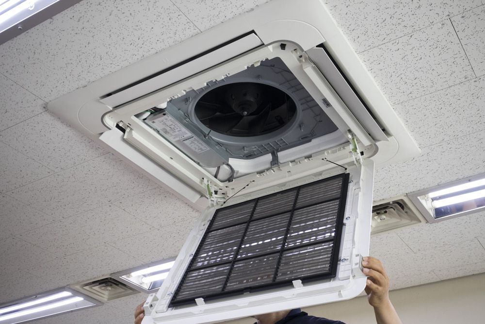 A Man Is Holding A Filter In Front Of An Air Conditioner — Climatech In Marcoola, QLD