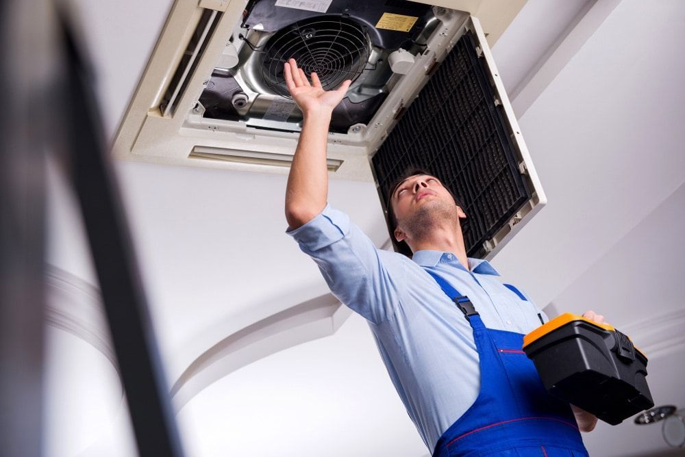 A Man Is Fixing An Air Conditioner On The Ceiling — Climatech In Marcoola, QLD