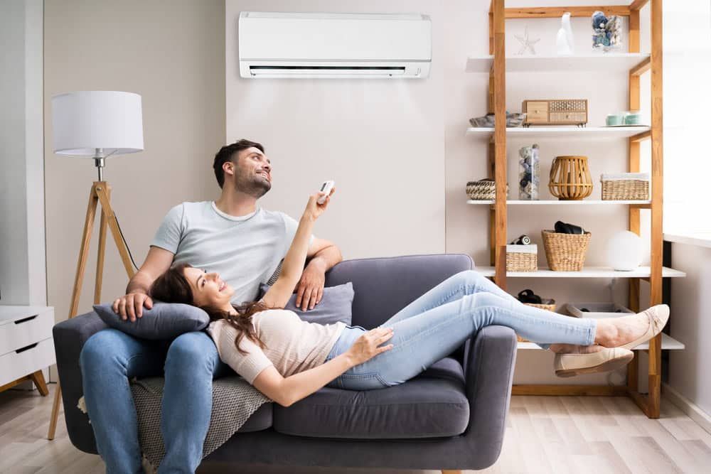 A Man And A Woman Are Sitting On A Couch In Front Of An Air Conditioner — Climatech In Marcoola, QLD