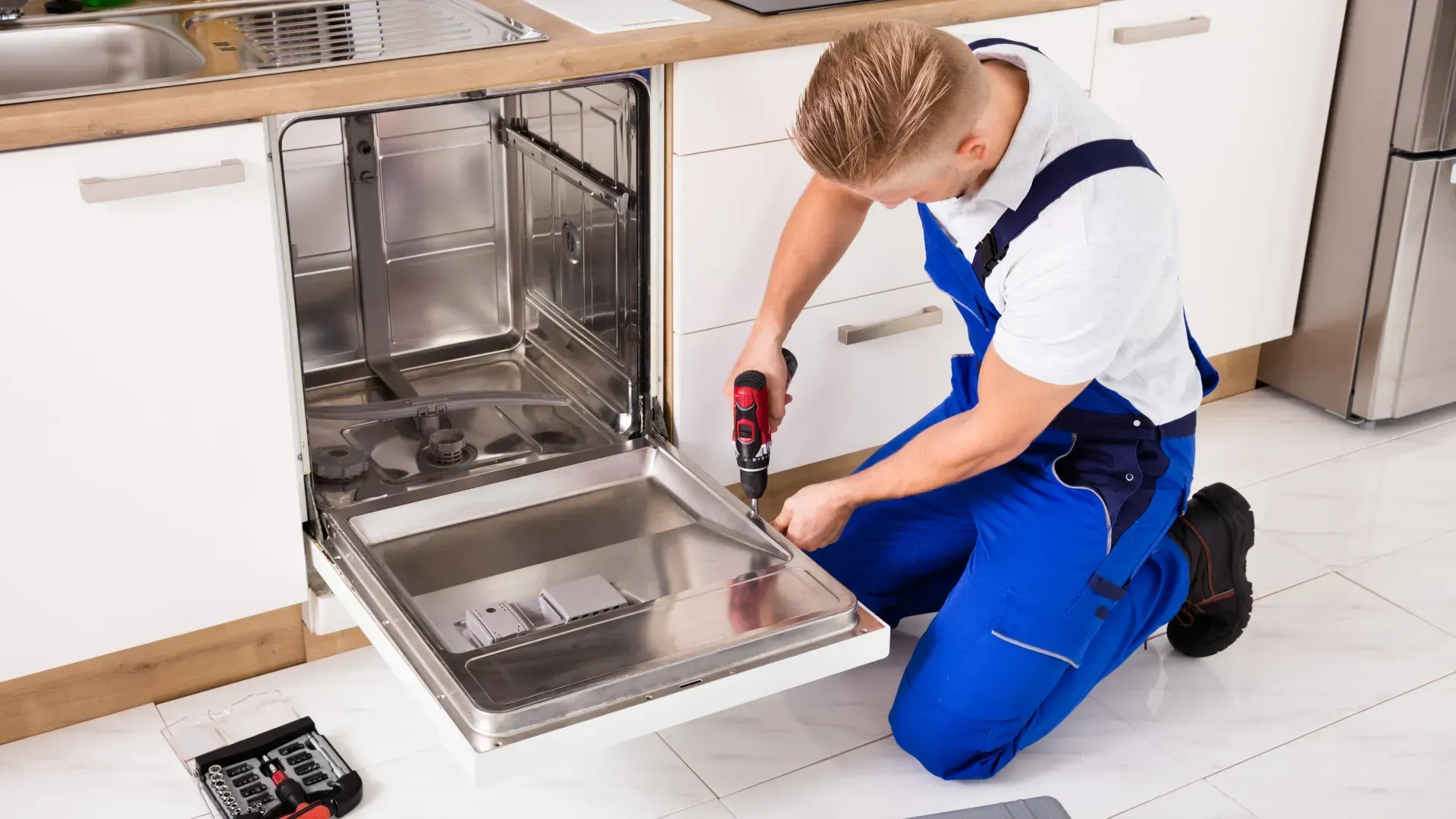 A man is fixing a dishwasher in a kitchen.