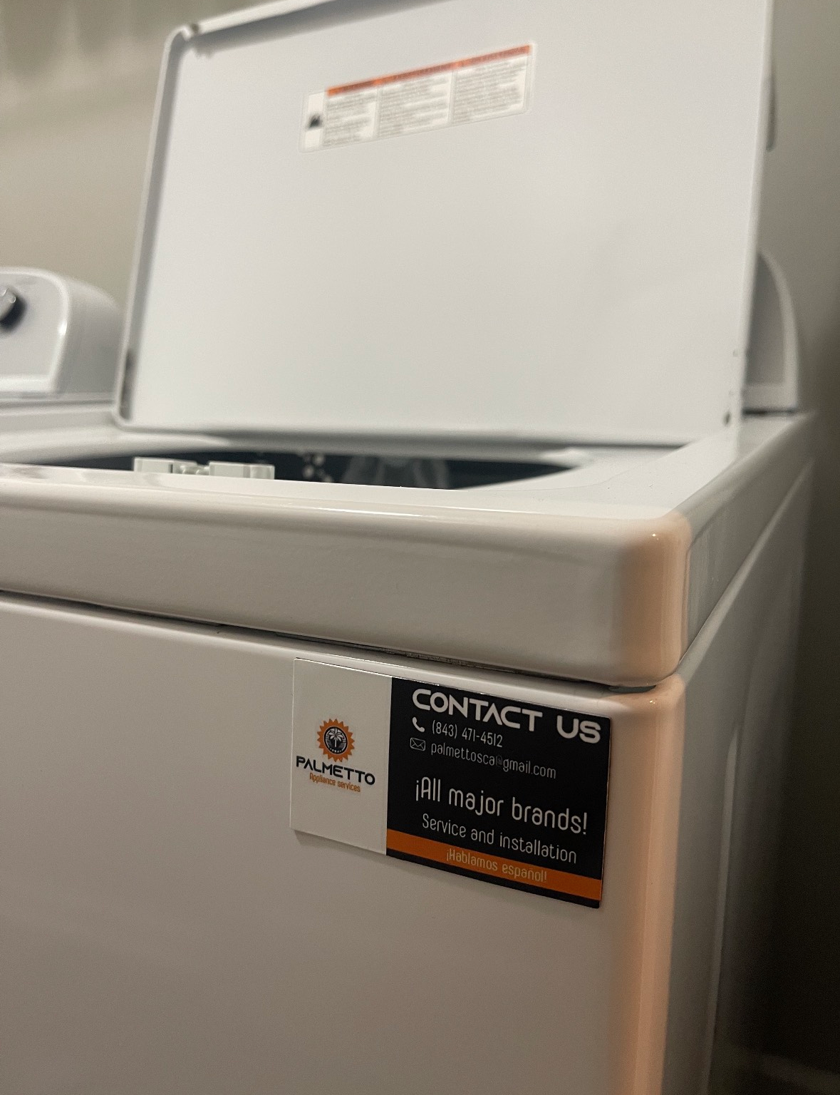 A white washing machine with the lid open and a contact us sticker on it.