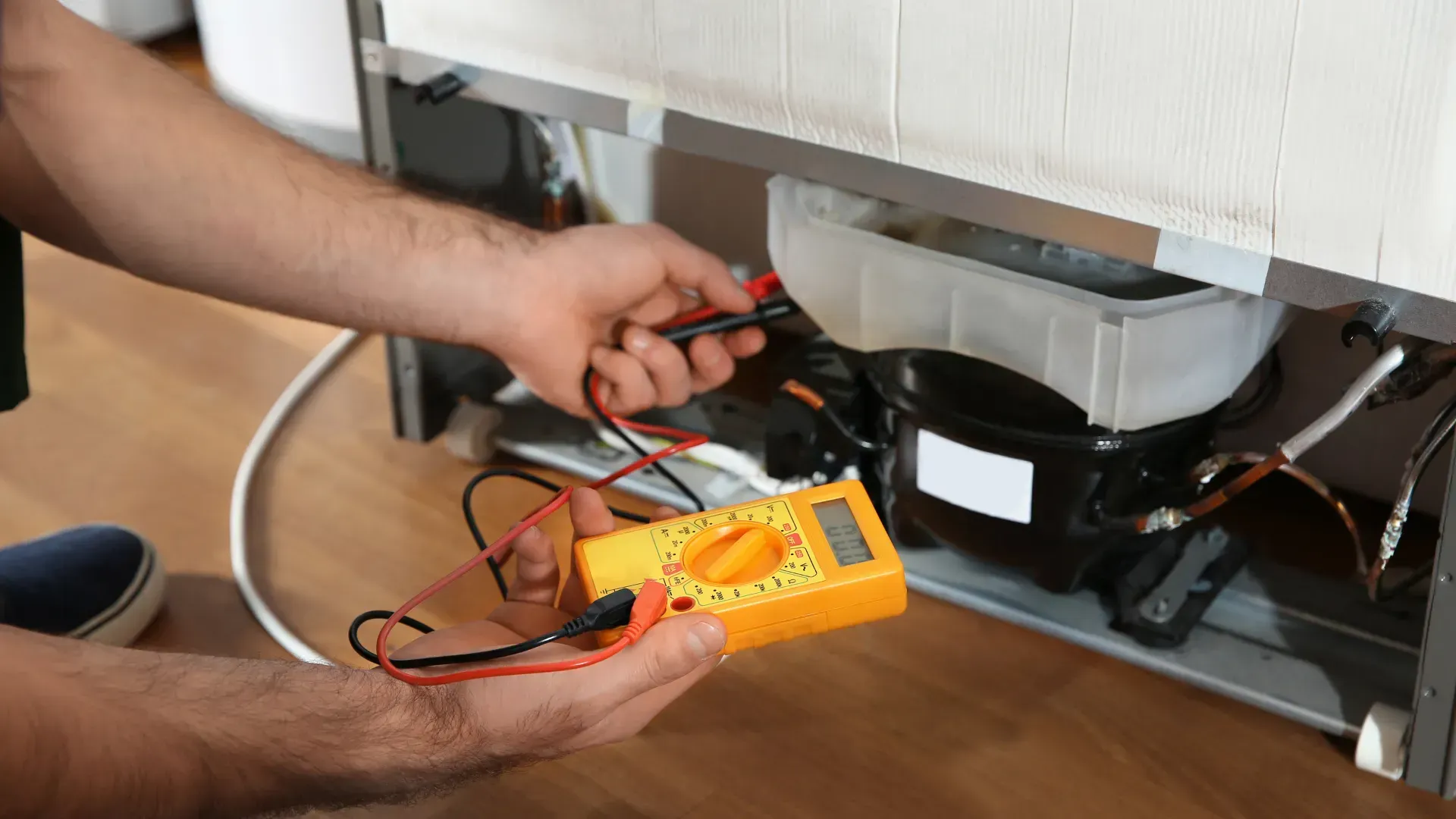 A man is using a digital multimeter to fix a refrigerator.