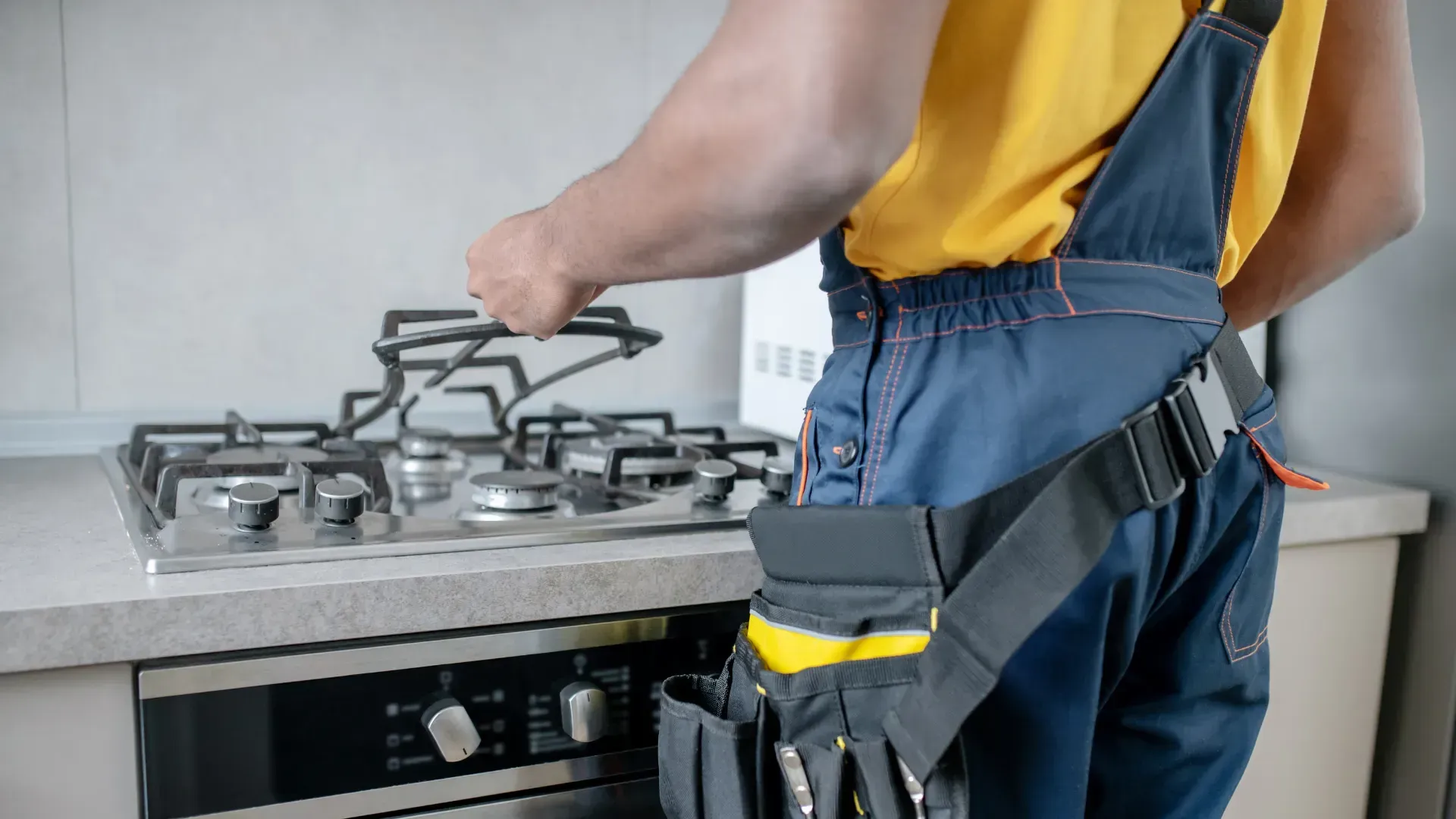 A man is fixing a gas stove in a kitchen.